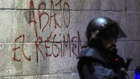 Graffiti says "Down with the regime" on Spain's parliament building near a riot officer during a protest before elections this month.