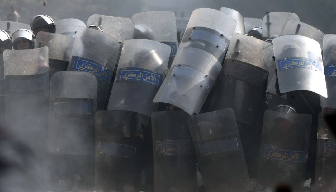 Riot police take cover behind their shields Wednesday during the fifth day of clashes with protesters near Tahrir Square.