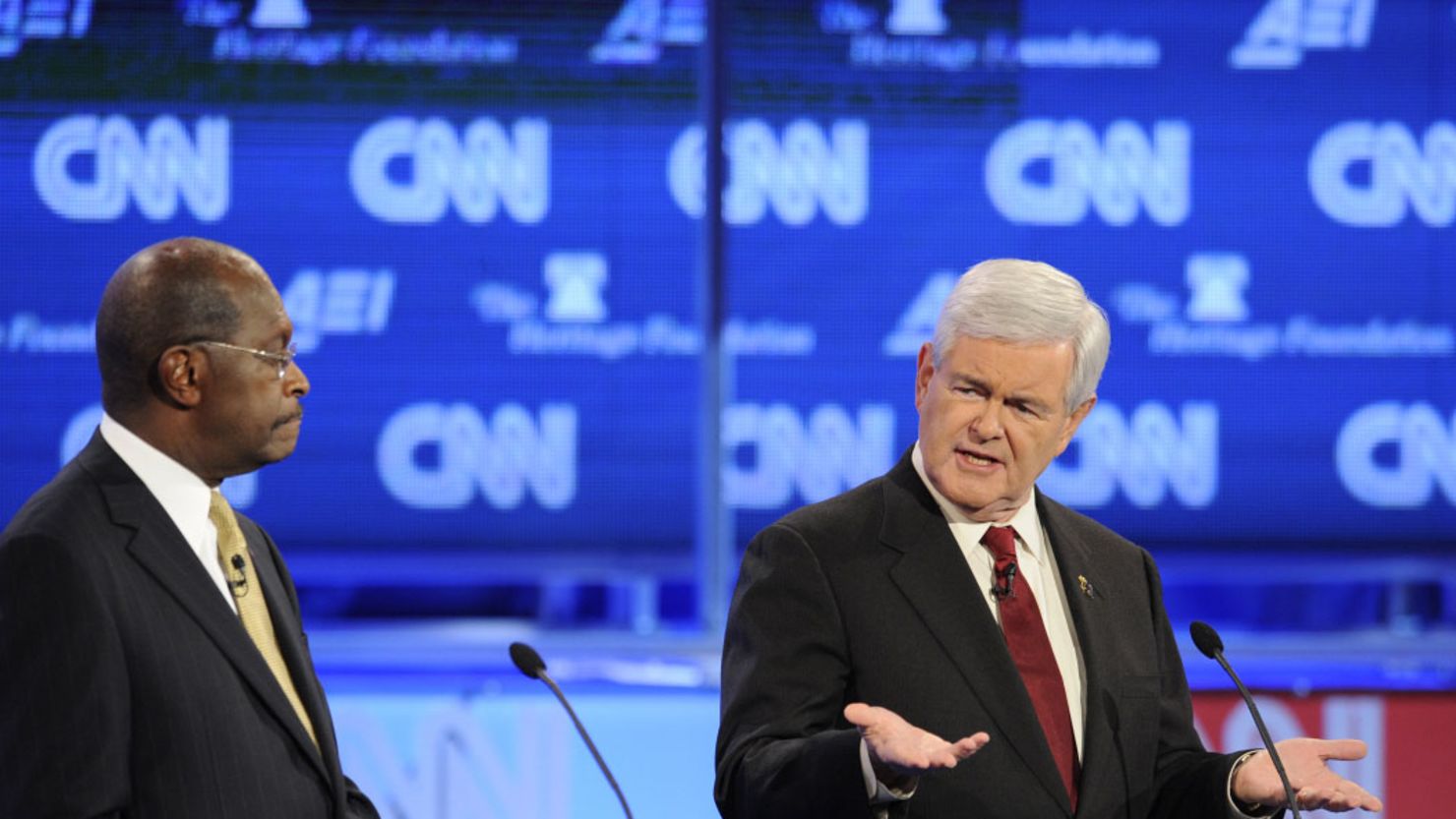 Herman Cain looks on as new GOP frontrunner Newt Gingrich speaks at CNN debate.