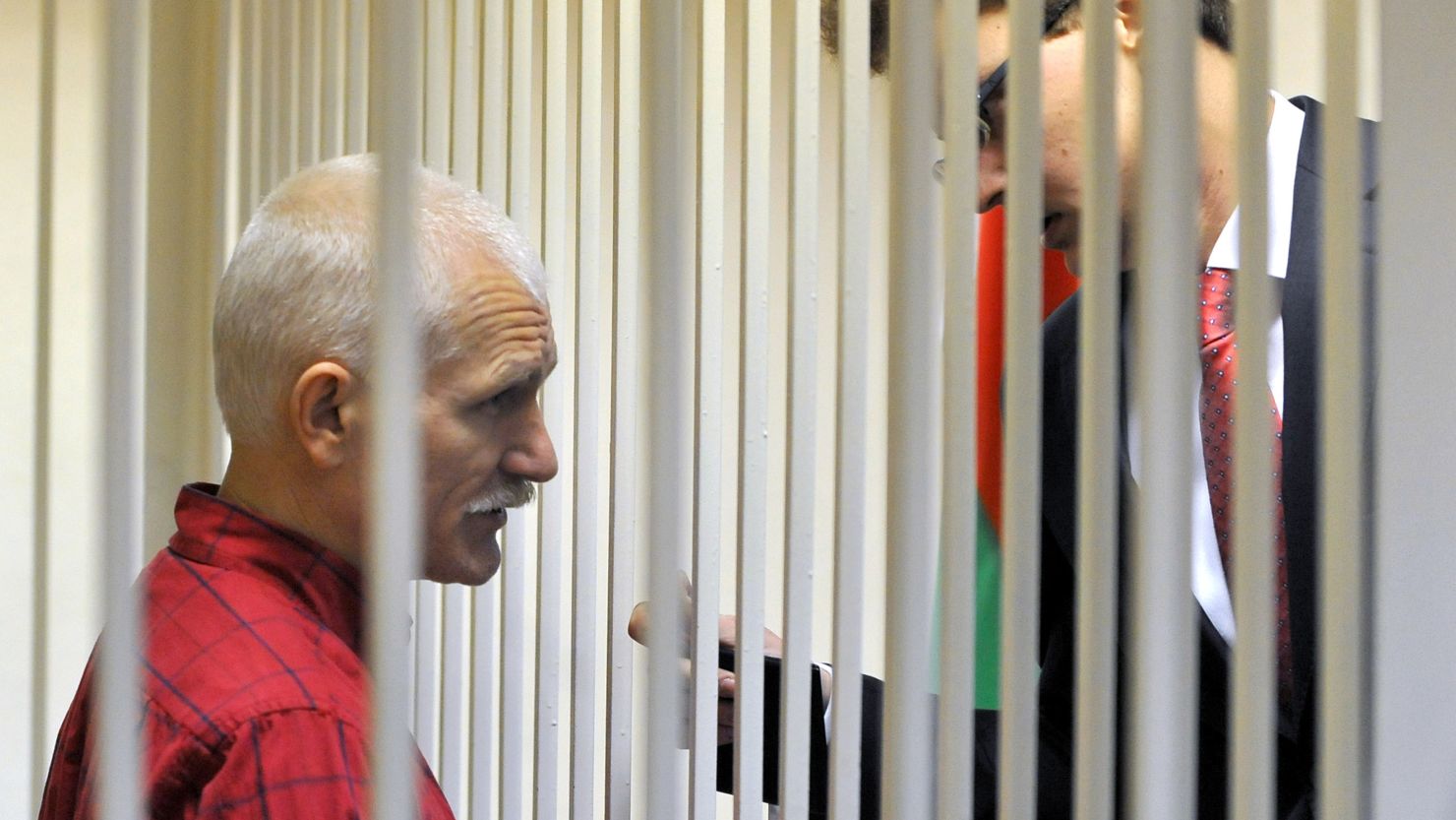 The head of Viasna Human Rights Center, Ales Bialiatski, speaks with his lawyer from the defendant's cage in a court in Minsk, on November 24, 2011.