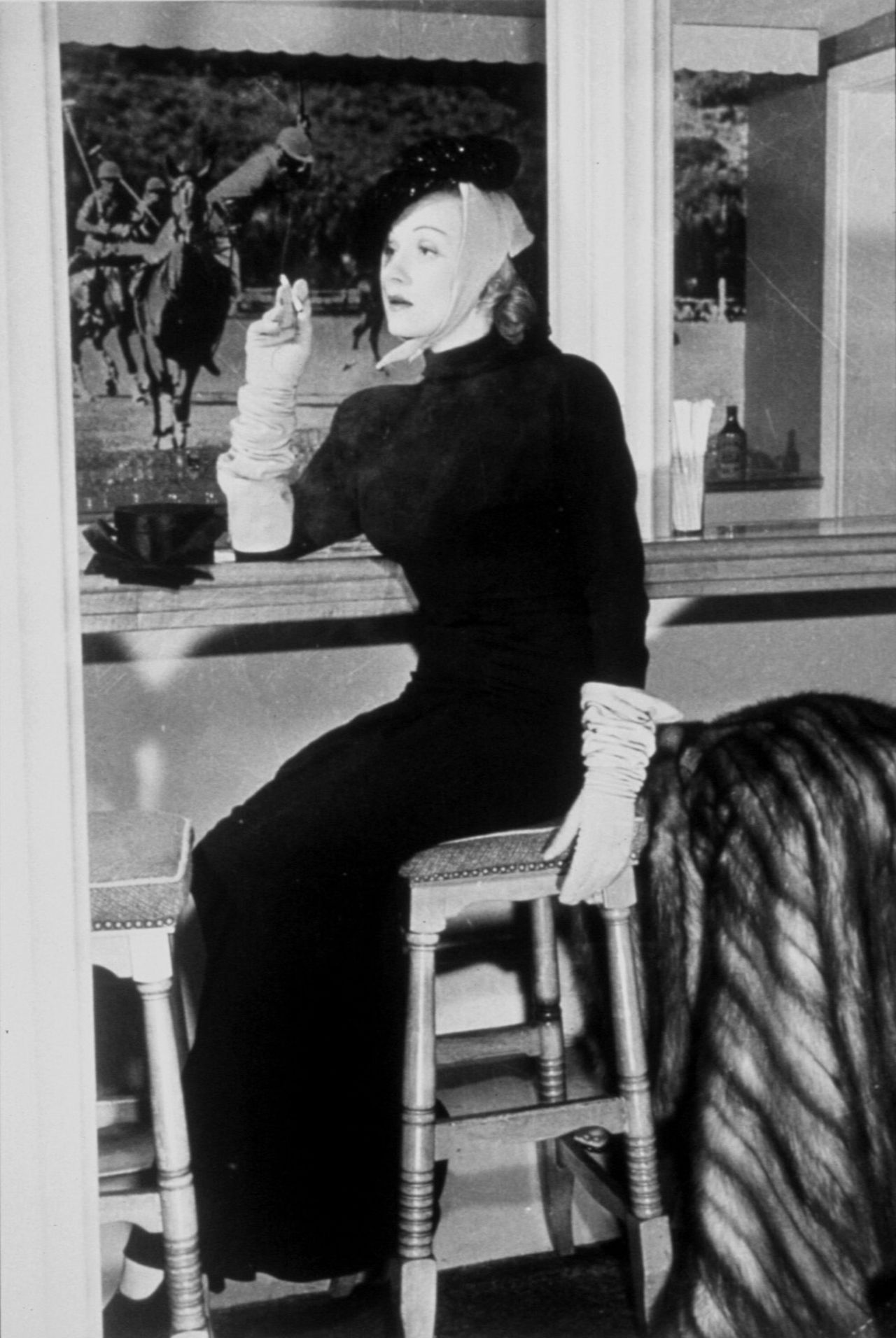 Marlene Dietrich convinced the Beverly Hills Hotel to ease its dress code so she could wear pants in the Polo Lounge. Behind her, the photo depicts a polo-playing Will Rodgers. 