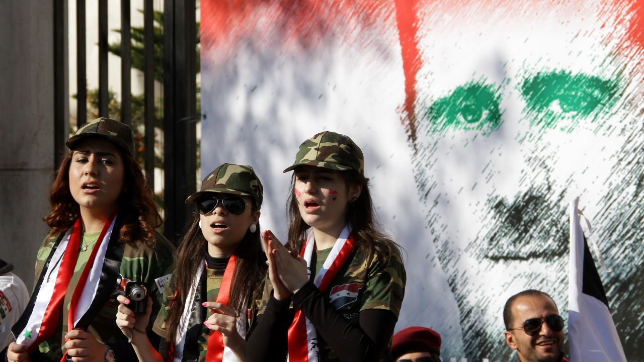Syrian pro-regime supporters dressed in military uniform stand in front of a mural of President Bashar al-Assad in Damascus on Saturday. 