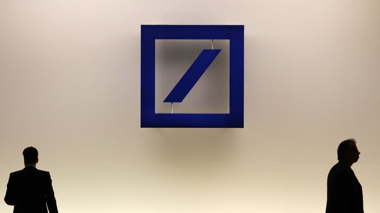 People walk by the logo of German company Deutsche Bank.