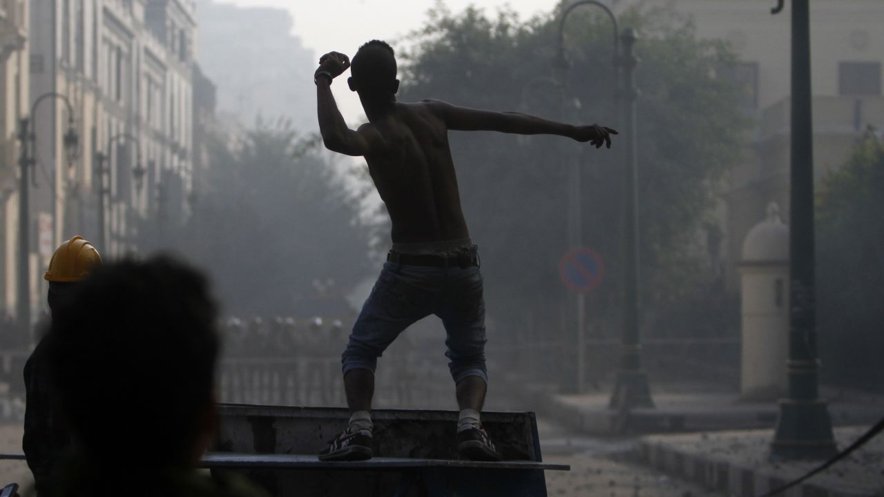 An Egyptian protester against continuing military rule throws stones at riot policemen during clashes in central Cairo Saturday.