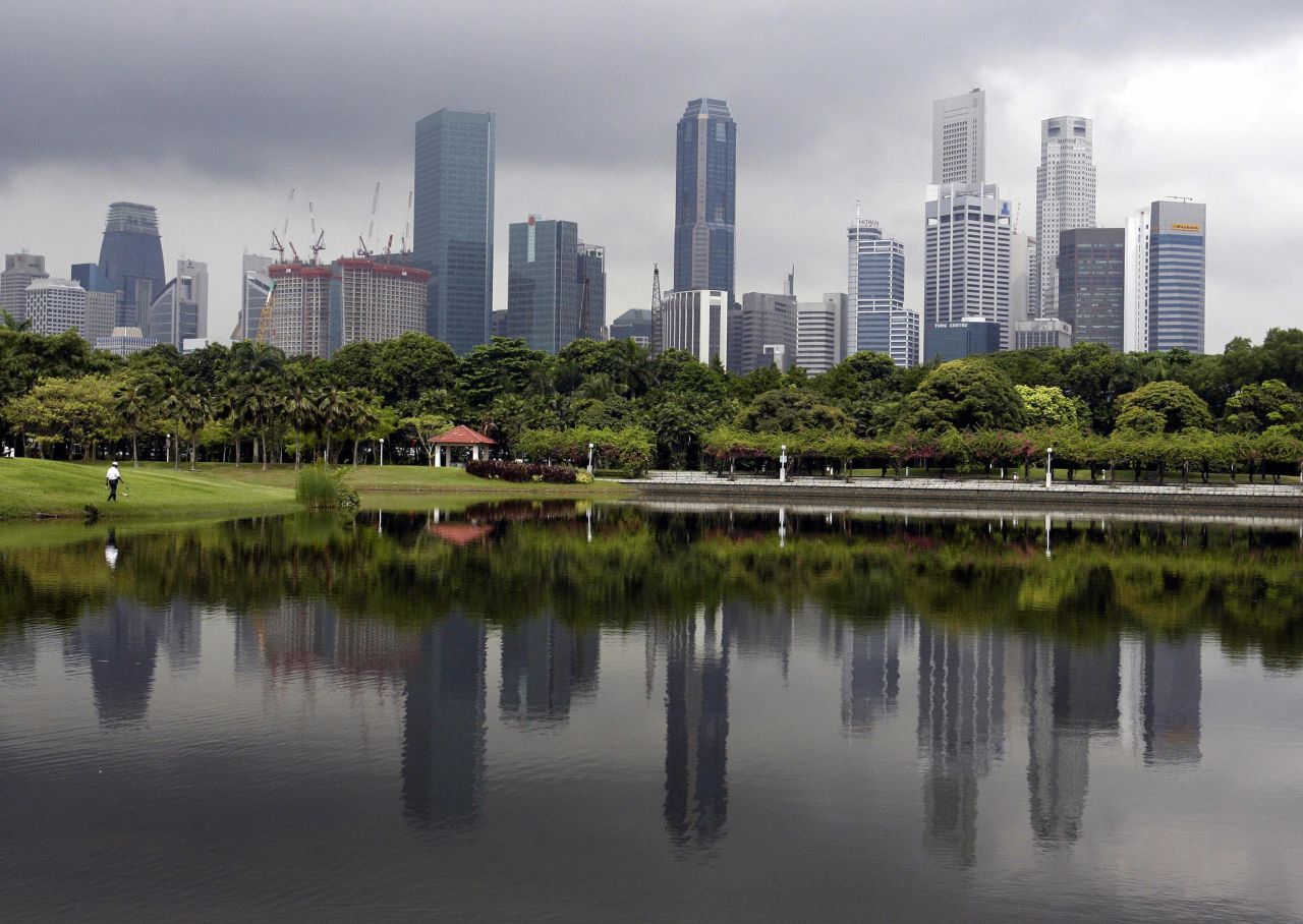 A crowded row of skyscrapers are reflected on a man-made lake while a dark cloud hovers in Singapore. Matthew Kahn, economics professor at the UCLA's Environment Institute, says that this type of high-rise, high-density urban living will be the norm in years to come, as cities adapt to migrants escaping their climate-ravaged homes.
