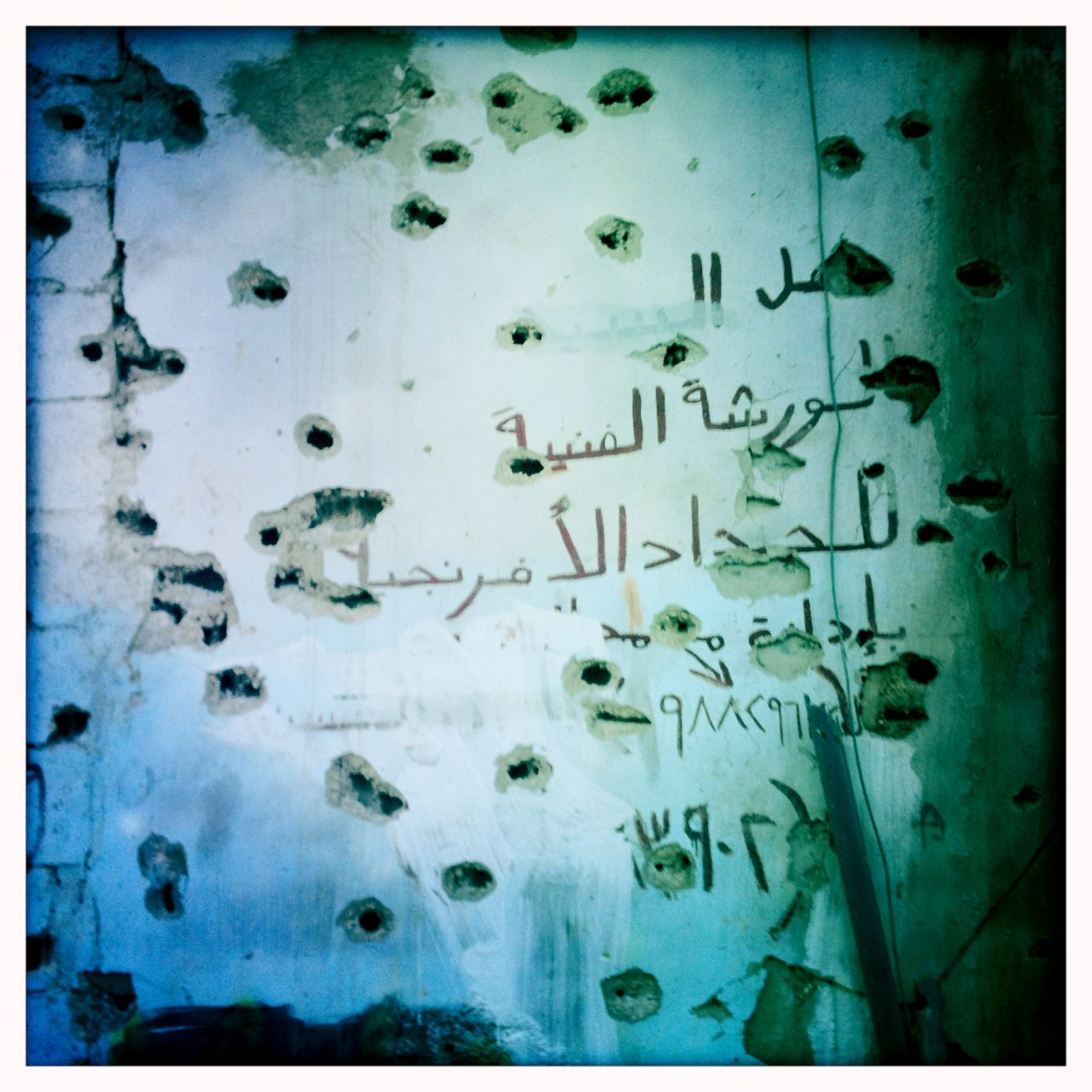 A bullet-marked wall is pictured in Baba Amr.