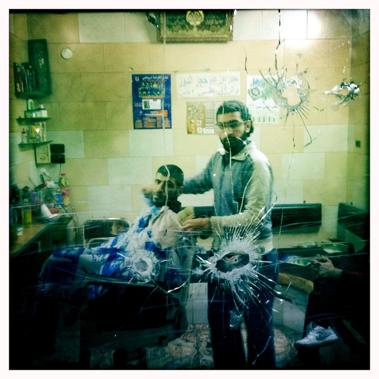 A barber stares through his bullet-marked window in the center of Baba Amr.