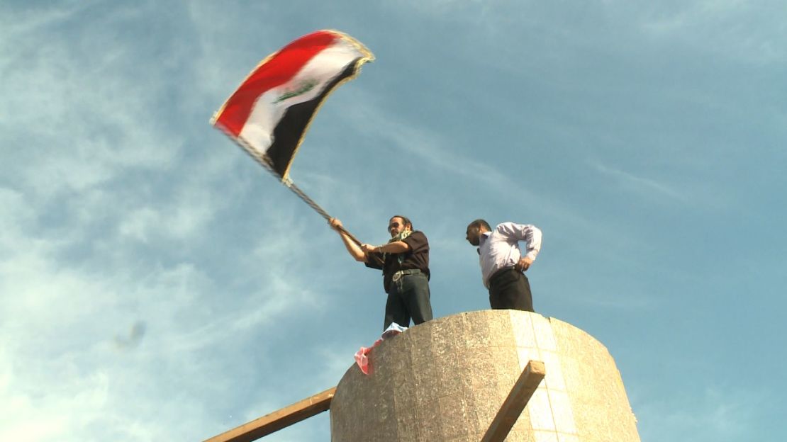 Dhirgham al-Zaidi, right, stands atop a pedestal that once held Saddam Hussein's statue as the Iraq flag is waved on Friday.