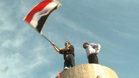 Dhirgham al-Zaidi, right, stands atop a pedestal that once held Saddam Hussein's statue as the Iraq flag is waved on Friday.
