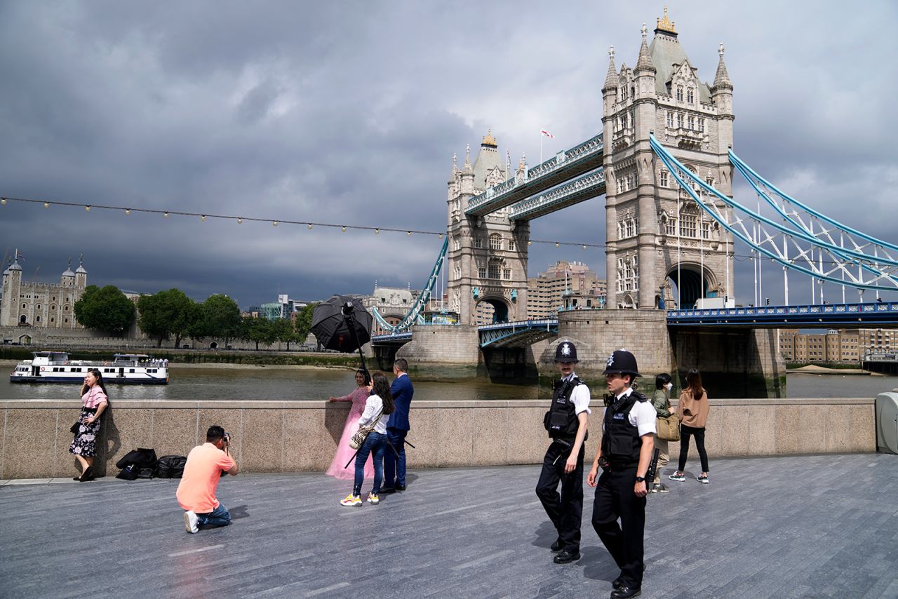 Policemen patrol near Tower Bridge as a bride is photographed on the bank of Thames river in London on Saturday, July 3. 