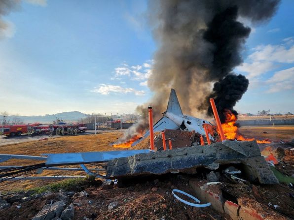 The crashed plane is engulfed in flames and smoke as firefighters work to put out the fire following the crash.