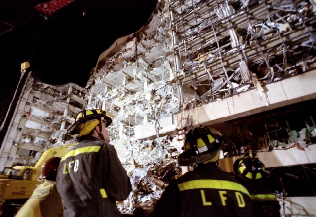 Firefighters examine the wreckage of the building as night falls on the day after the bombing.