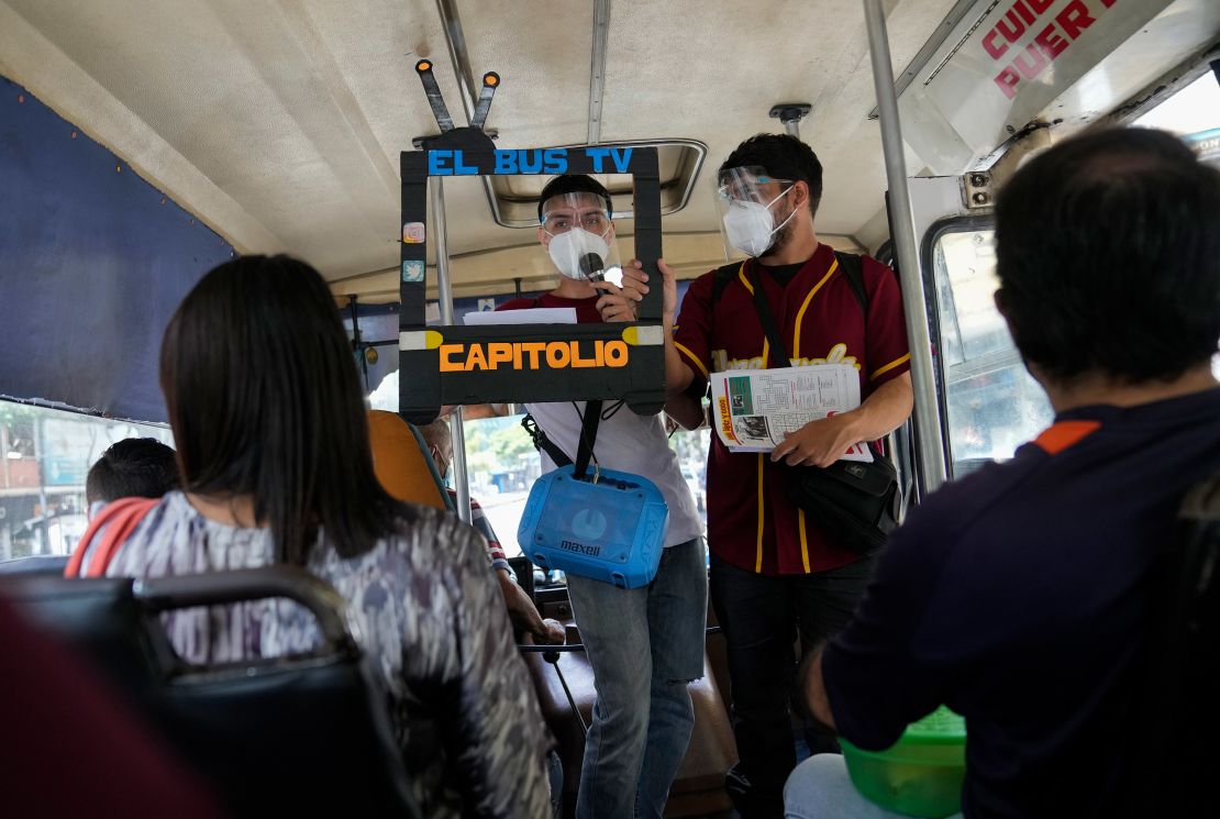 Juan Pablo Lares, right, holds a cardboard frame in front of his associate Maximiliano Bruzual who reads their newscast "El Bus TV Capitolio" to commuters on a bus in Caracas, Venezuela, Saturday, July 31, 2021.
