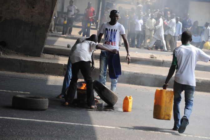 Bystanders watch as protestors try to set fire to a car tire in the middle of Ikorodu Road in Lagos.