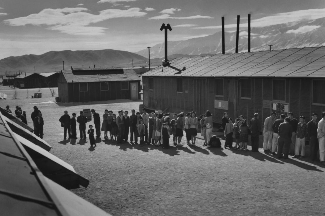  People wait in a line in front of a building at midday at a Japanese internment camp in 1943.