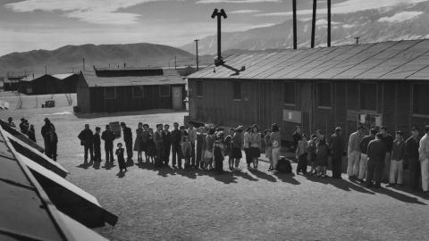  People wait in a line in front of a building at midday at a Japanese internment camp in 1943.