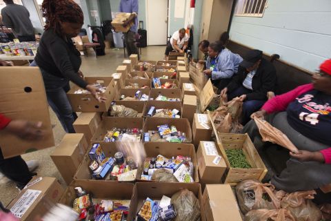 Members pack boxes with a hodgepodge of items ranging from cereal and canned goods to cleaning supplies. 