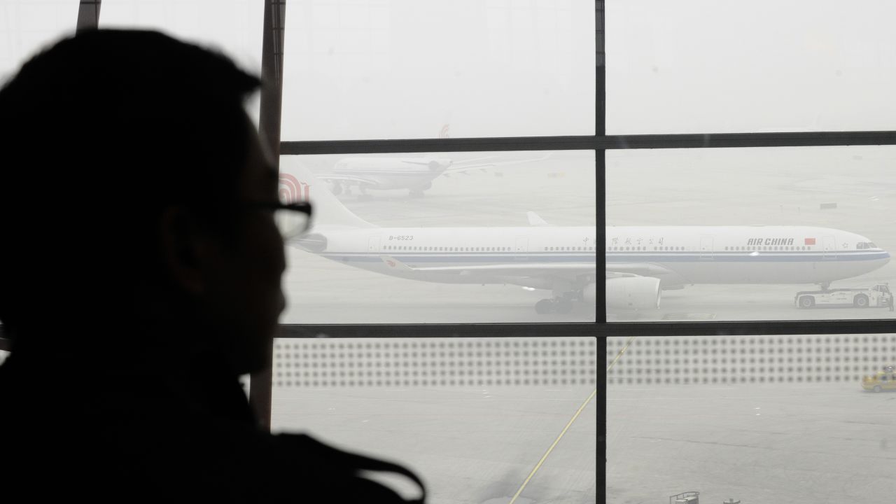 A traveller looks out at an airplane shrouded in smog at Beijing International Airport on December 5, 2011.