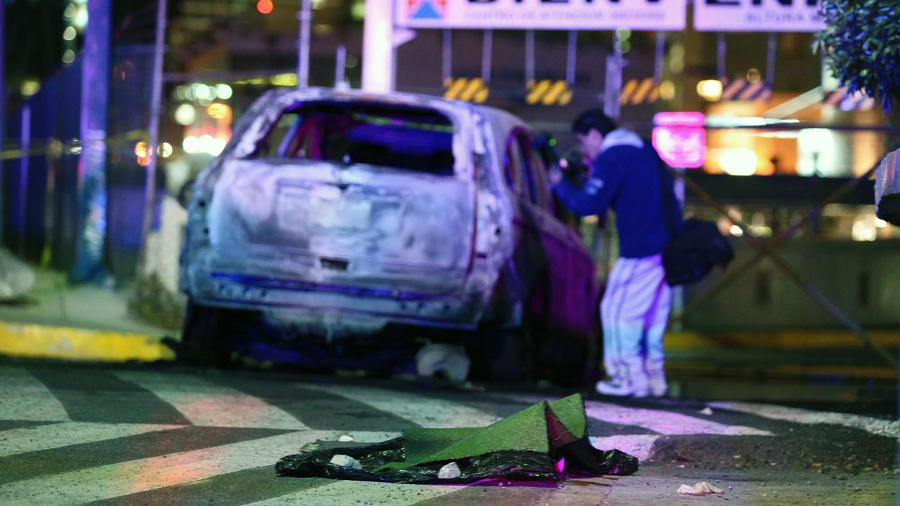 A forensic team member photographs victims found inside a burnt car on January 11. Two heads are covered by a carpet.