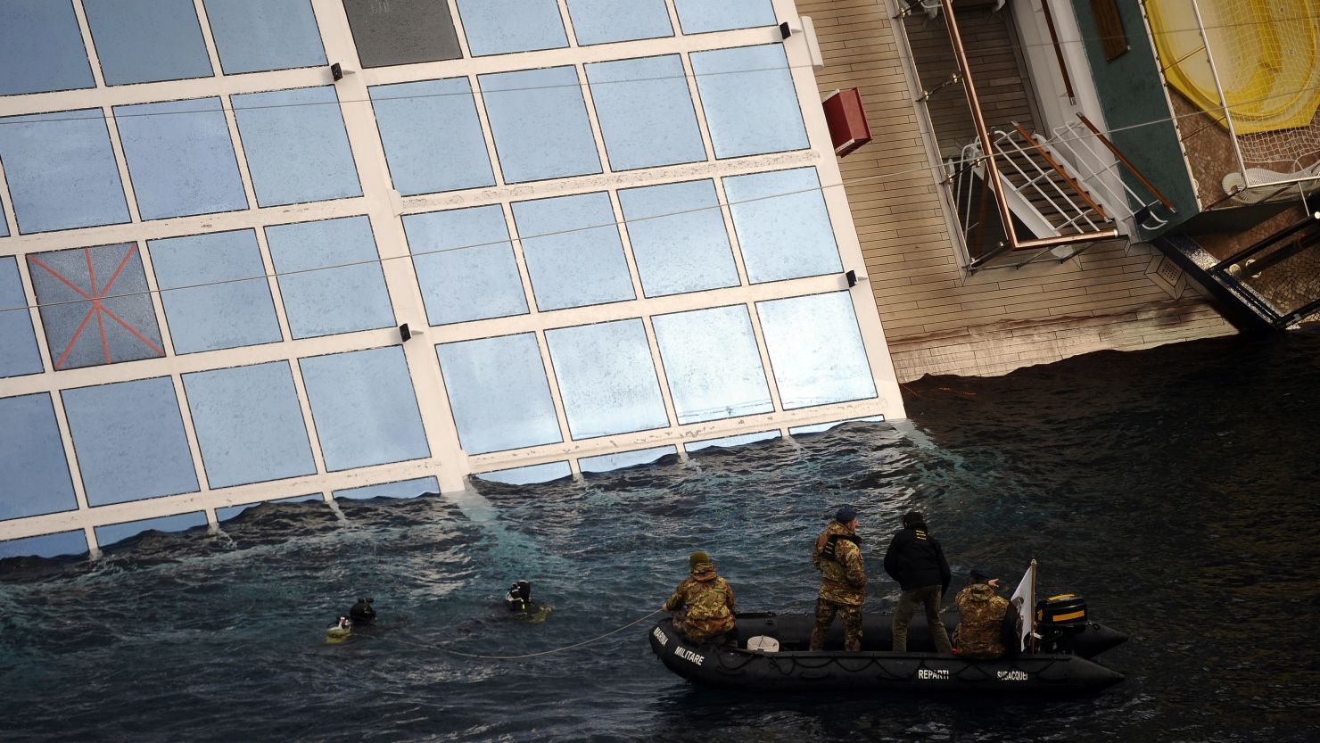 Divers inspect the Costa Concordia on Sunday. The death toll  from the disaster off the Tuscan island stands at at least six.