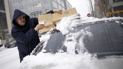 A man scrapes snow from the back window of his car in downtown Seattle on Wednesday.