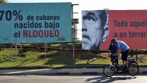 In Cuba, a man checks his motorcycle in front of political billboards that allude to the US embargo on Cuba