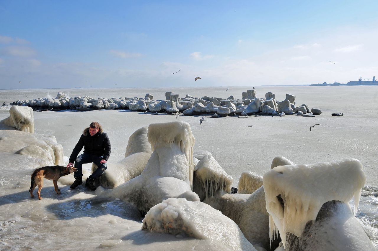 A man pets a dog next to frozen sea waters in Constanta, Romania, on Wednesday. Temperatures plunged to -34 degrees Celsius (-29 degrees Fahrenheit) in central Romania.