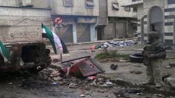 A Syrian rebel stands next to a destroyed government forces tank bearing the rebel-adopted revolution flags in Homs.