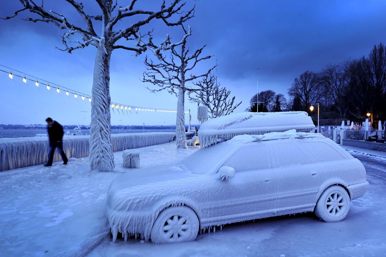 A man walks past an ice-covered car Sunday on the frozen waterside promenade at Lake Geneva in Versoix, Switzerland.