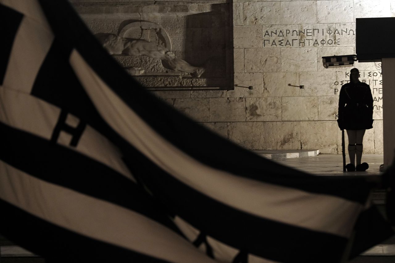 A Greek Presidential guard stands guard behind a Greek flag at the tomb of the Unknown soldier in front of the parliament during a demonstration in Athens 
