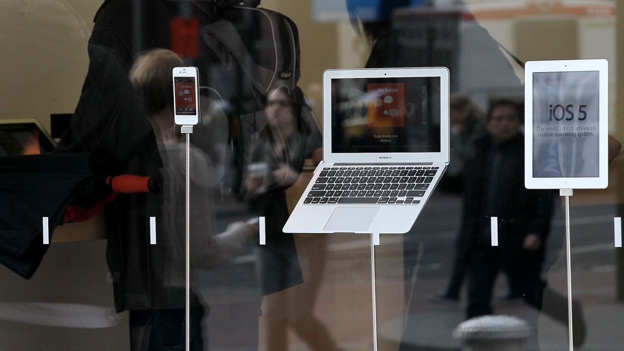 A Macbook Air laptop, an iPad 2 and an iPhone sit on display in a store window. 