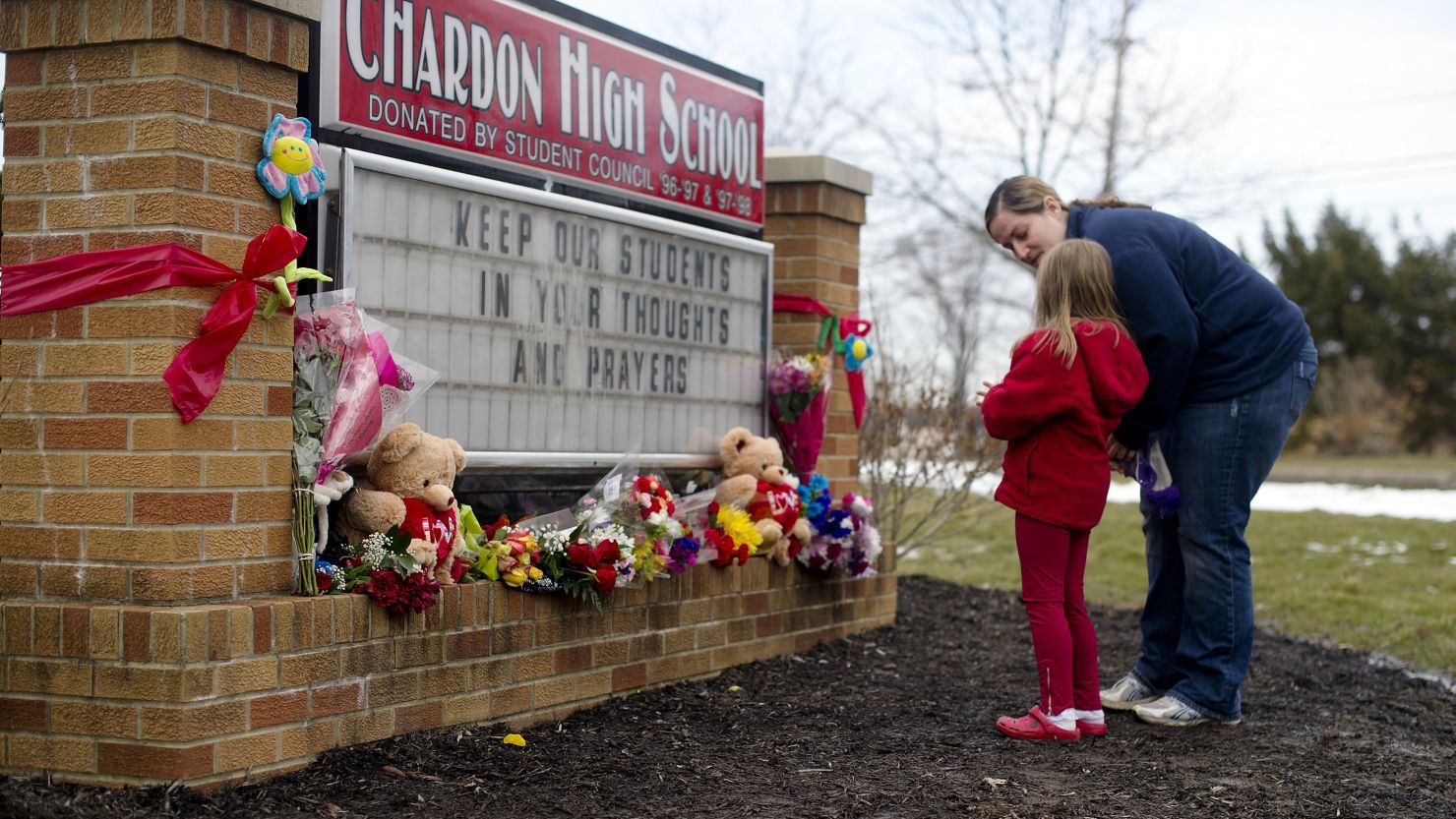 Angela May and her daughter, Eleanore, 5, of Chardon place flowers on the sign outside Chardon High School.
