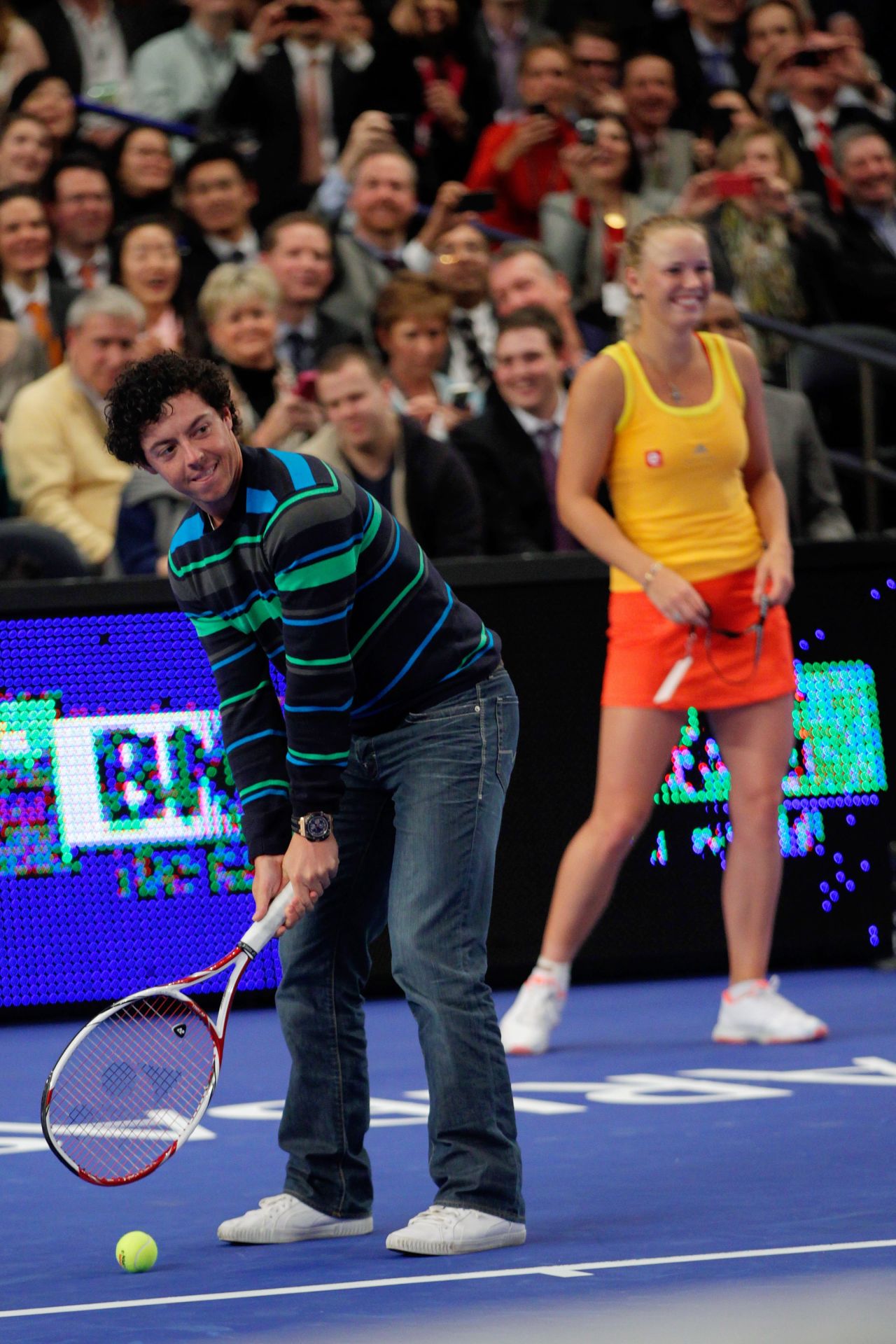 Wrong sport Rory ! McIlroy addresses a tennis ball golf style with Maria Sharapova at the other end.