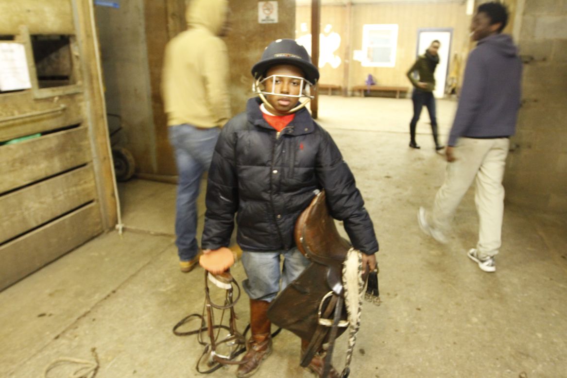 Brian Ferrell makes his way through the stable wearing his polo helmet and towing his horse's saddle. Ferrell, 13, joined Work To Ride five years ago. Ferrell, alongside his fellow riders, gets to ride horses in exchange for cleaning out stalls and brushing down horses. 
