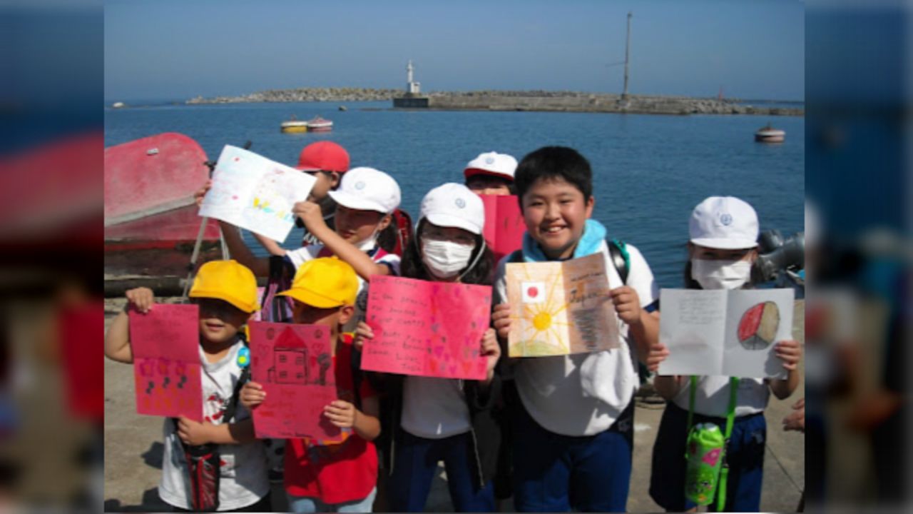 Cards from the project bring bright smiles to the faces of elementary school children in Iwaki City, Japan, as they gathered on the city pier just down from their destroyed school on the four-month anniversary of the earthquake and tsunami.