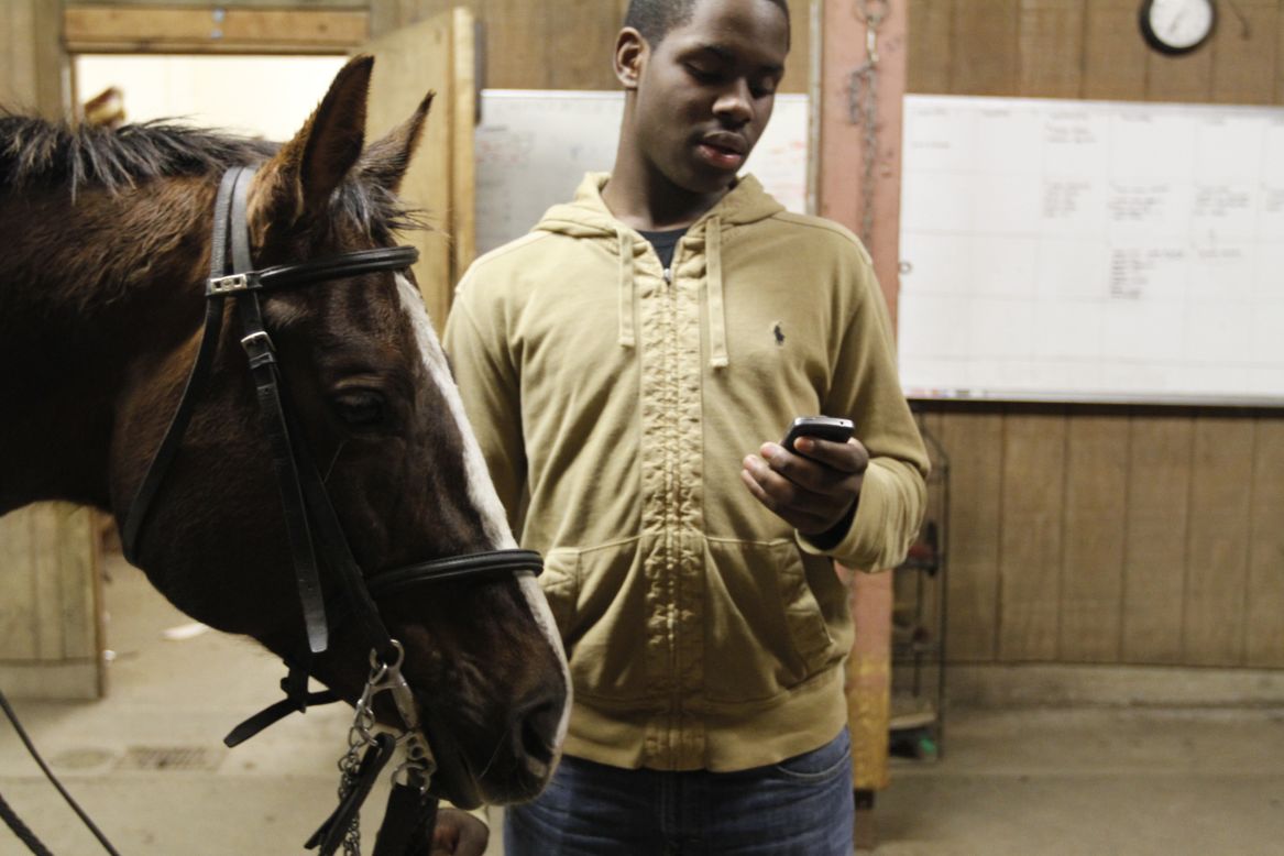 Sixteen-year-old Brandon Rease checks his cell phone while waiting for the others to finish tacking their horses. Rease, had to walk several blocks in the rain from the bus stop to reach the stable. "In my neighborhood and all of our neighborhoods, there's normal day-to-day violence, drug dealing and kids around a bunch of negativity. When you come to the barn or travel, all of that is washed away and you can be a kid."  
