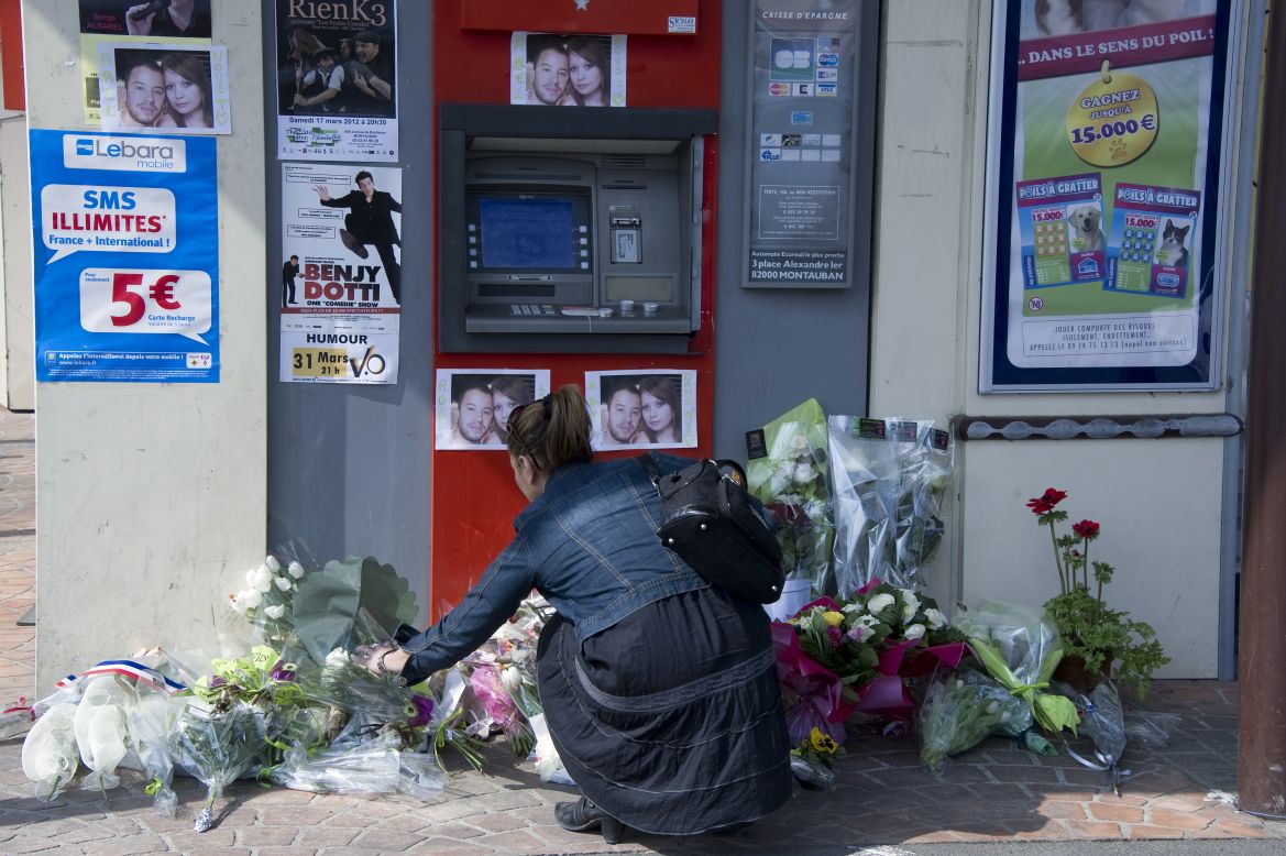 A woman places a bouquet of flowers on March 17, at the site where two French soldiers were killed on March 15, in the French city of Montauban.