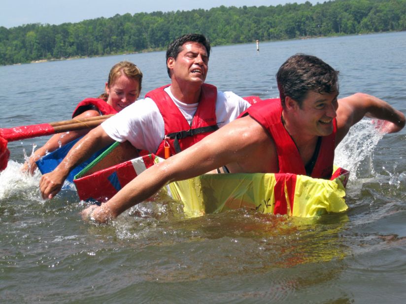 Executive participants strain to stay afloat as they attempt to cross a lake in a vessel they have built on an Adventure Associates retreat in North Carolina, USA.