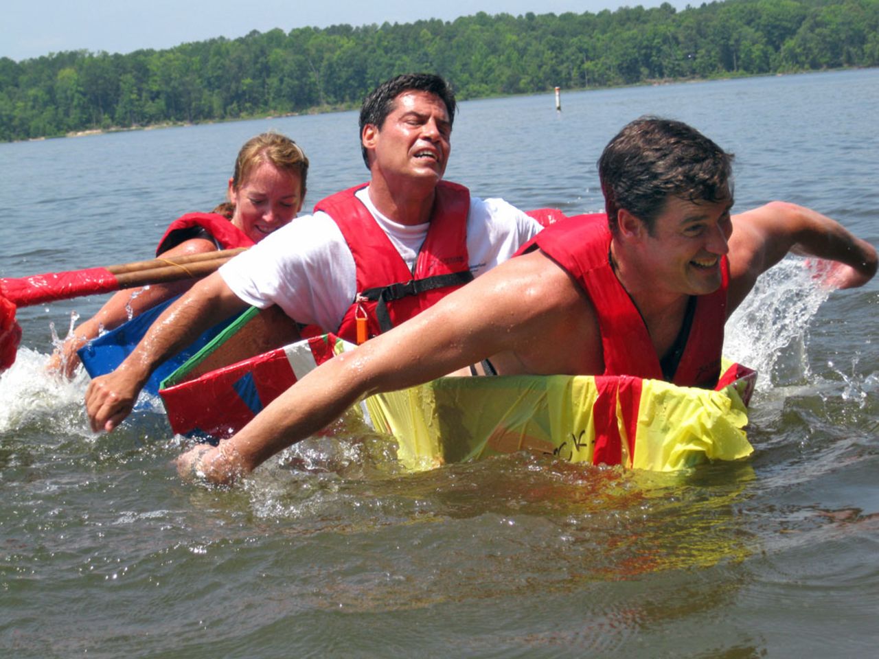Executive participants strain to stay afloat as they attempt to cross a lake in a vessel they have built on an Adventure Associates retreat in North Carolina, USA.