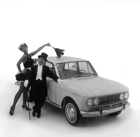 A man stands next to his Datsun  while a woman dressed as a French maid dusts the roof of the vehicle, circa 1966.