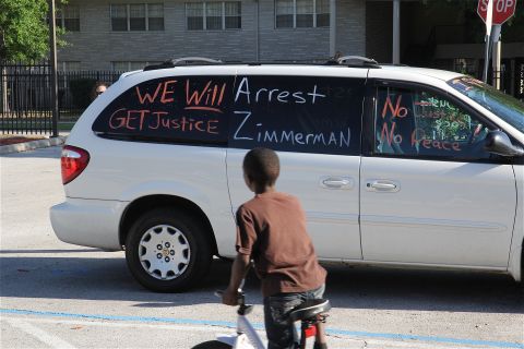 A protest sign painted on the window of a car at a housing project calls for Zimmerman's arrest. For some, the Martin case has become a rallying cry, a chance to air what they believe are years of grievances. 