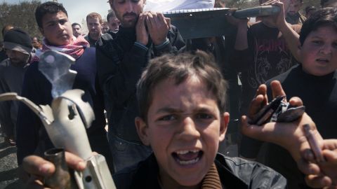 Mourners carry the coffin of Ahmad Qarush, 13, who was killed in Shermin. A boy holds up remains of Syrian Army shells.