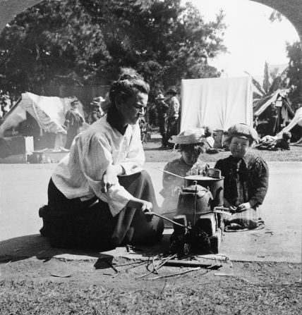 A refugee from the 1906 San Francisco earthquake prepares a meal over a makeshift stove at the  Army-run Golden Gate Park relief camp. In the background, soldiers and other refugees stand near tents set up for living quarters. An estimated 225,000 people were left homeless after the earthquake and subsequent fires.