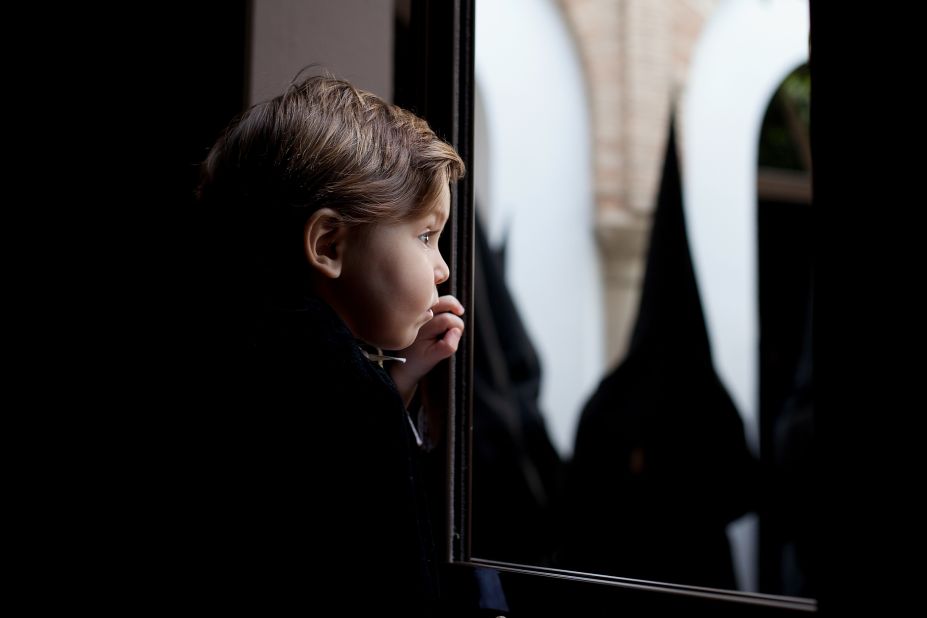 From a window, a child watches penitents of the Dolores brotherhood before a procession Friday during Holy Week.