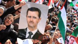 A Syrian woman holds a picture of President Bashar al-Assad as other protestors fly Palestinian and pre-Baath Syrian flags during a demonstration to mark Land Day in Damascus on March 30, 2012.