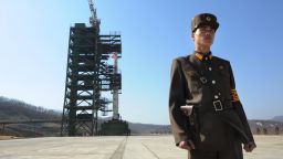 A North Korean soldier stands guard in front of a rocket that is being readied for launch