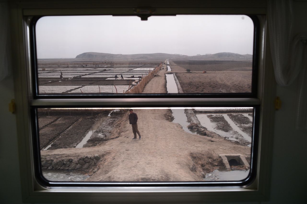 Workers and farms are seen through the window of a train as it passes through the country.