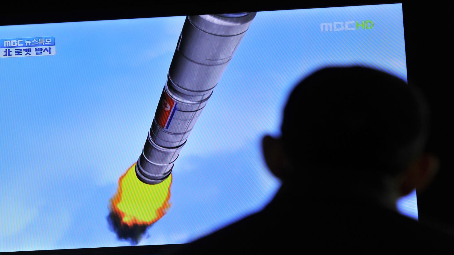 South Koreans at a train station in Seoul watch a TV screen showing a graphic of North Korea's rocket launch Friday.