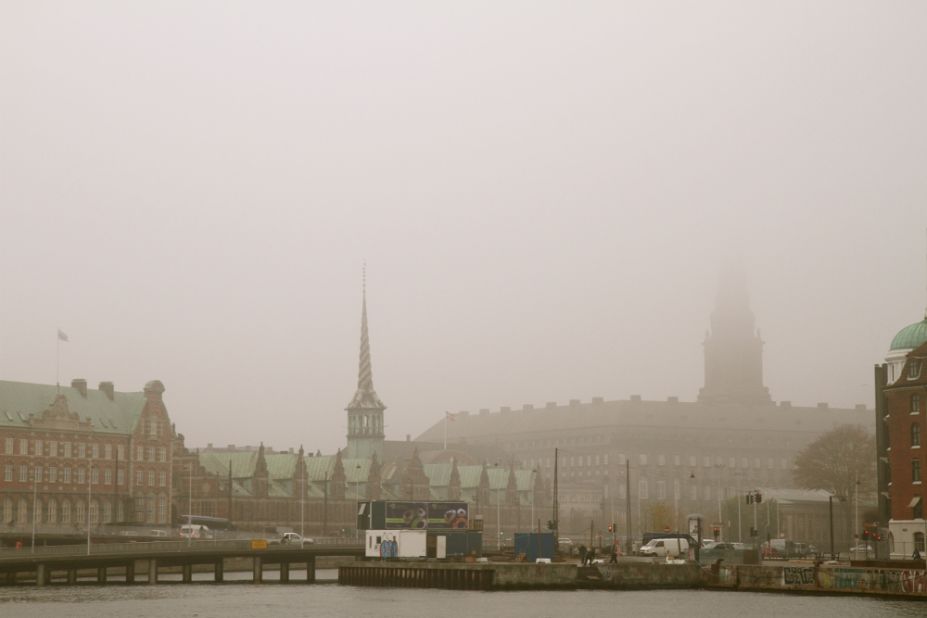 Mist shrouds the 17th-century spires of Copenhagen Harbor, a striking contrast to the sweltering streets of Mumbai. 