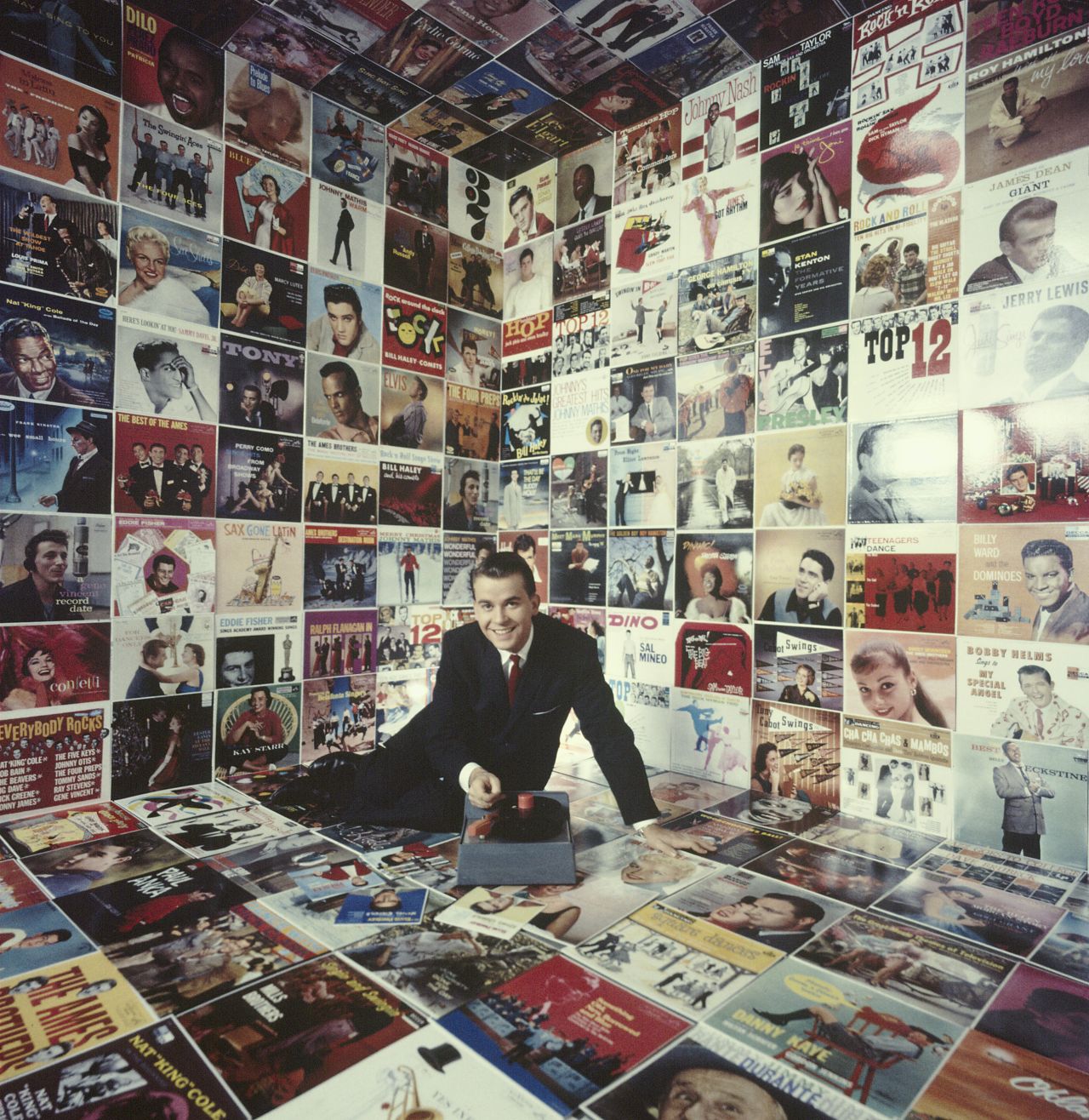 Clark sits in a room decorated floor to ceiling with record album covers circa 1958.